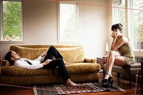 Person lying on couch while partner looks concerned
