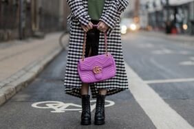 A woman wears black boots, a plaid coat, and holds a pink Gucci bag. 