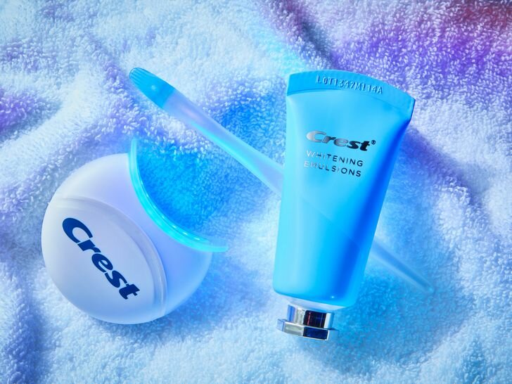 The whitening paste tube, applicator and LED light for the Crest Whitening Emulsions LED Teeth Whitening Kit on a towel