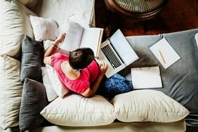 View from above of a person sitting on a couch working on their laptop with books scattered about