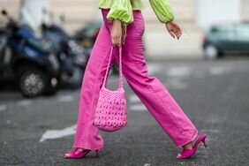 A woman wears colored jeans with a matching knit bag and pink shoes.