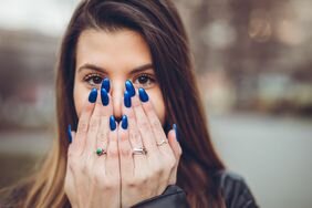 Young brunette woman holding her hands to her face to show off her royal blue nails