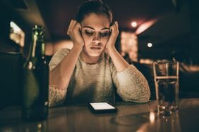 Unhappy person sitting at a bar with hands on the side of their head looking down at their phone