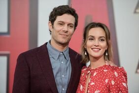 Adam Brody in a gray shirt and dark blazer and Leighton Meester in a red dress with white print