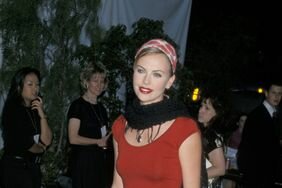 Charlize Theron wearing a white tea length skirt, red top, and black scarf in 2000