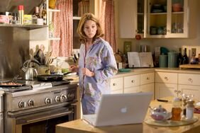 Diane Lane cooking in the kitchen looking at her laptop