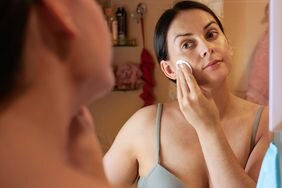 Person looking in mirror and applying a cotton pad to face