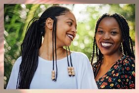 Two Black women smiling at one another with braided hairstyles