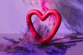 A pink heart sits among a background of purple with splatters of colorful powder.