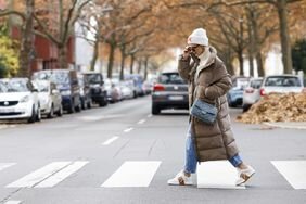 Person crossing the street in a long puffer coat, jeans, and white beanie