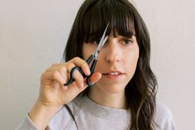 Person with medium-length brown hair cutting their bangs with scissors