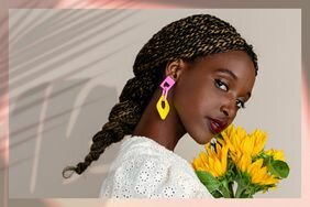 Dark skinned person with their natural hair braided, wearing colorful earrings and holding flowers