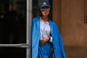 Woman wears blue blazer and skirt and navy Yankees hat