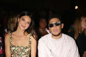 Kendall Jenner in a floral dress alongside Devin Booker in sunglasses at a fashion show