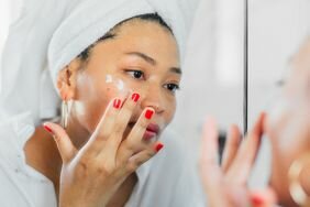 A woman applying moisturizer to her face.