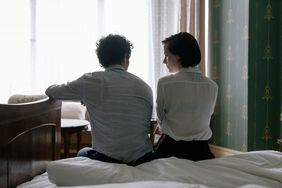 A couple sitting on the edge of the bed looking at each other