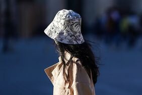 A passerby wears a white with black flower pattern bucket hat.